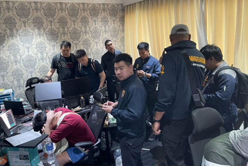 Police officers inspecting seized laptops and mobile phones laid out on a table during a raid
