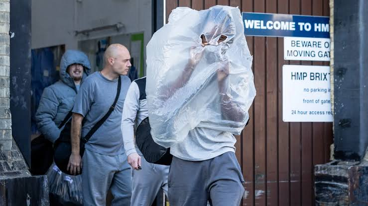 People leaving a prison gate carrying bags, being greeted by family and media