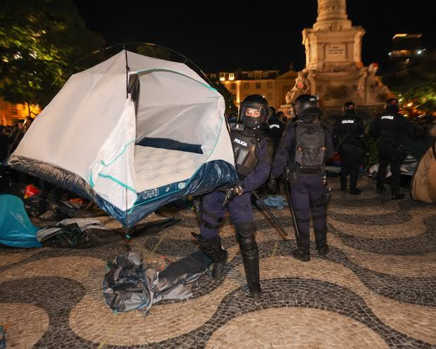 Police officers dismantling protest tents in a European city square as protesters look on
