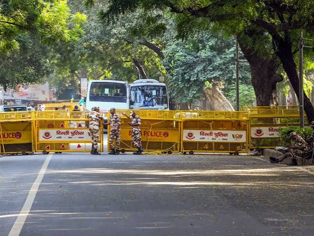 Commuters at a Delhi Metro station with barricades and police visible ahead of a protest