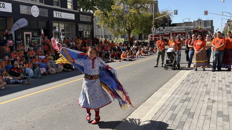 Orange shirts laid out at a community memorial with Indigenous artwork in the background
