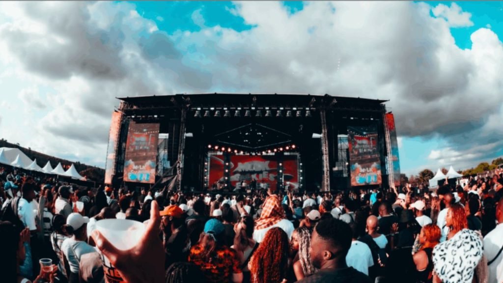 Crowd at a South African outdoor music festival at dusk, stage lights and people dancing