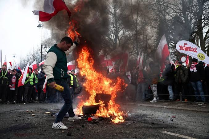Protesters in Poland with signs and umbrellas at night; Polish flag visible.